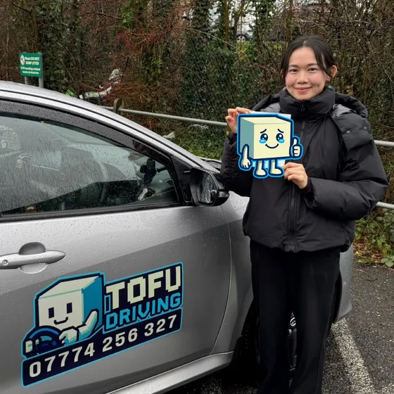 Gigi - A TOFU Driving student celebrating passing the driving test next to the instructor's car